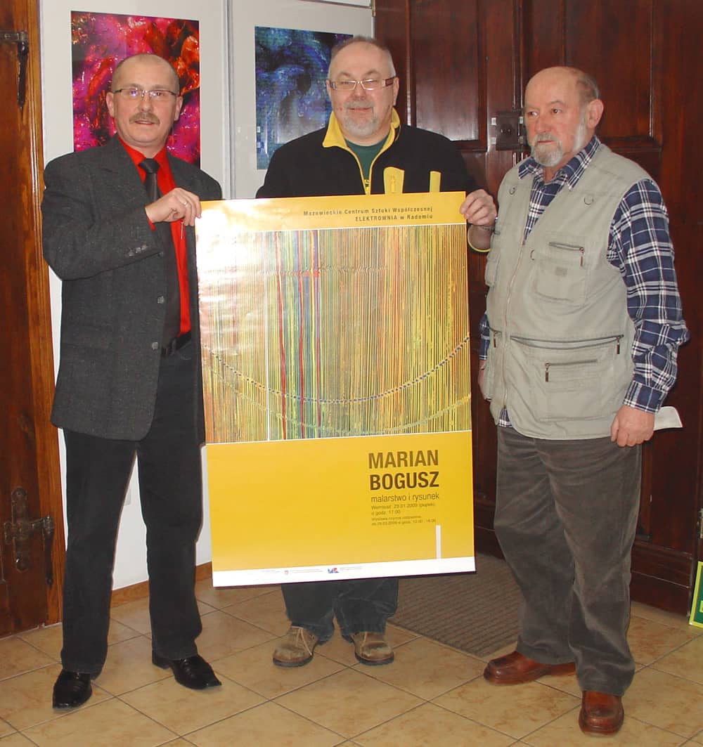 Na zdjęciu trzech mężczyzn trzymających plakat wystawy